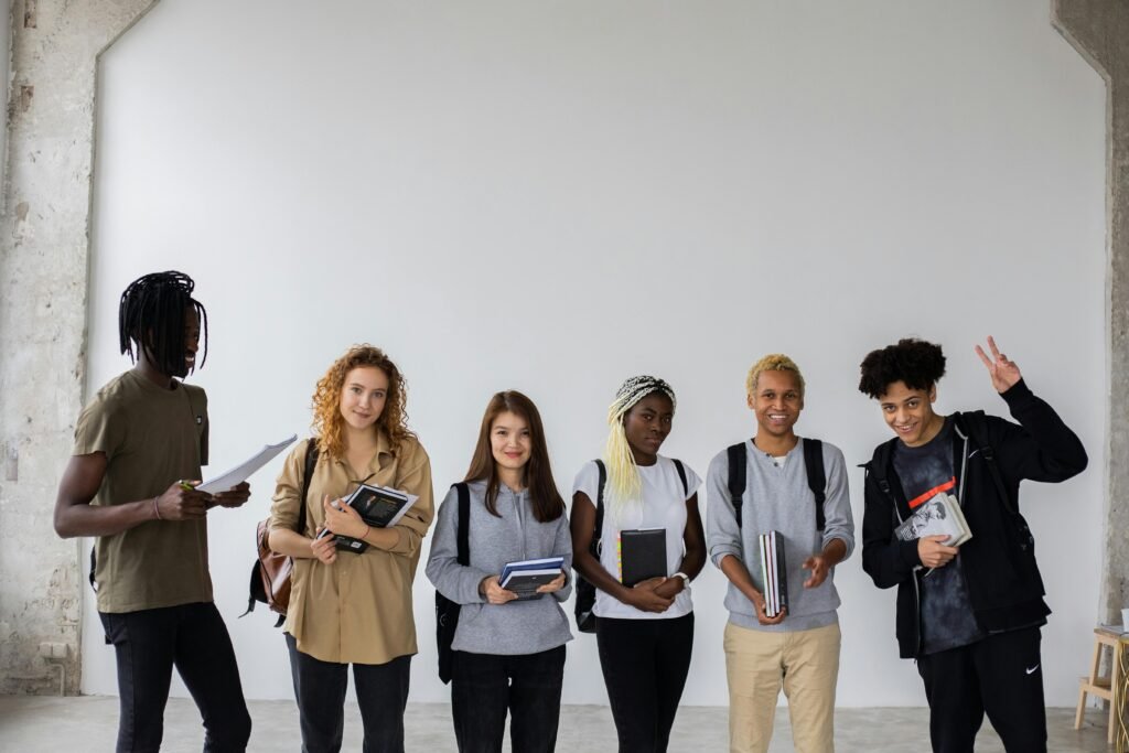 A group of cheerful, diverse college students posing together with books indoors.